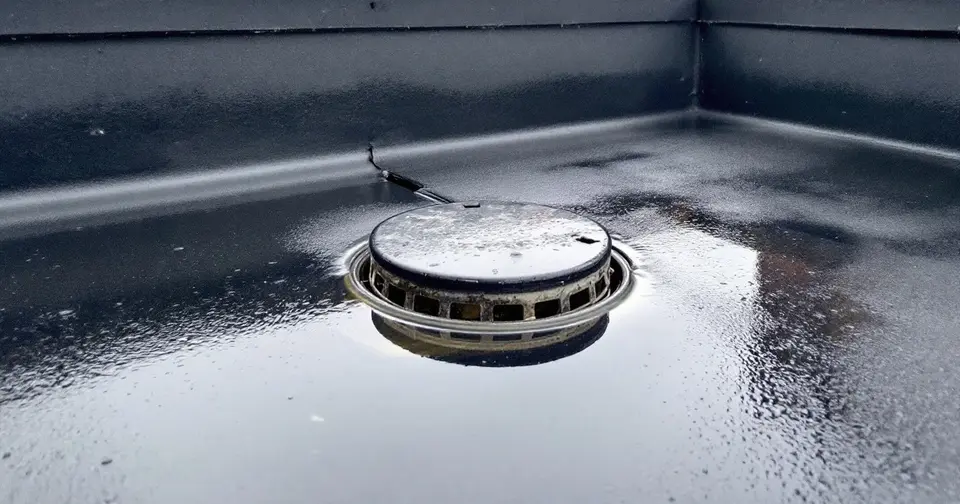 Plat dak na een regenbui met een plas water rond de dakafvoer en een donkere opstaande rand