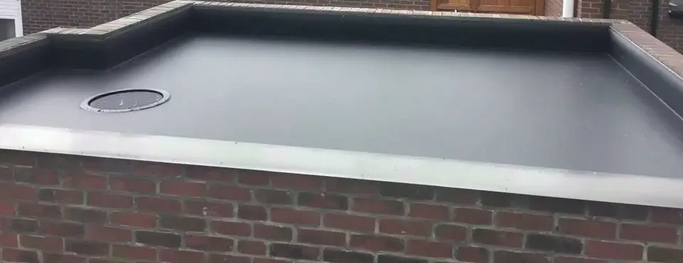 Plat dak van een aanbouw met nieuwe zwarte EPDM, een aluminium daktrim op de gemetselde dakrand en een ronde afvoer